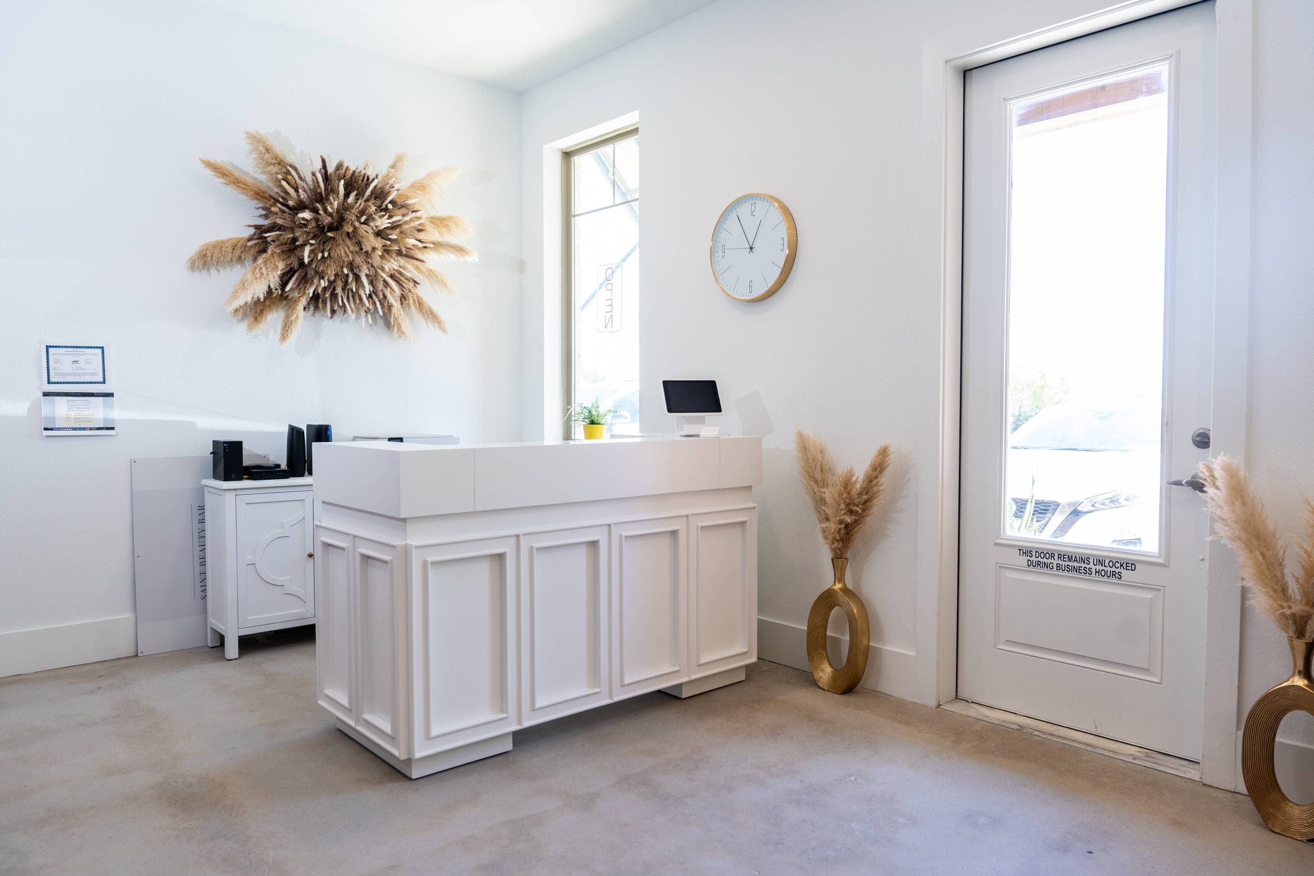 The white reception desk, with dried pampas grass and a wall clock