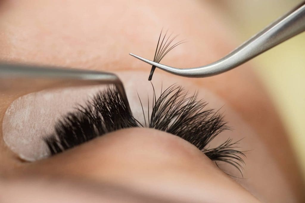 Saint Beauty Bar lash artist applying lash extensions on client — natural, full lashes with soft background.