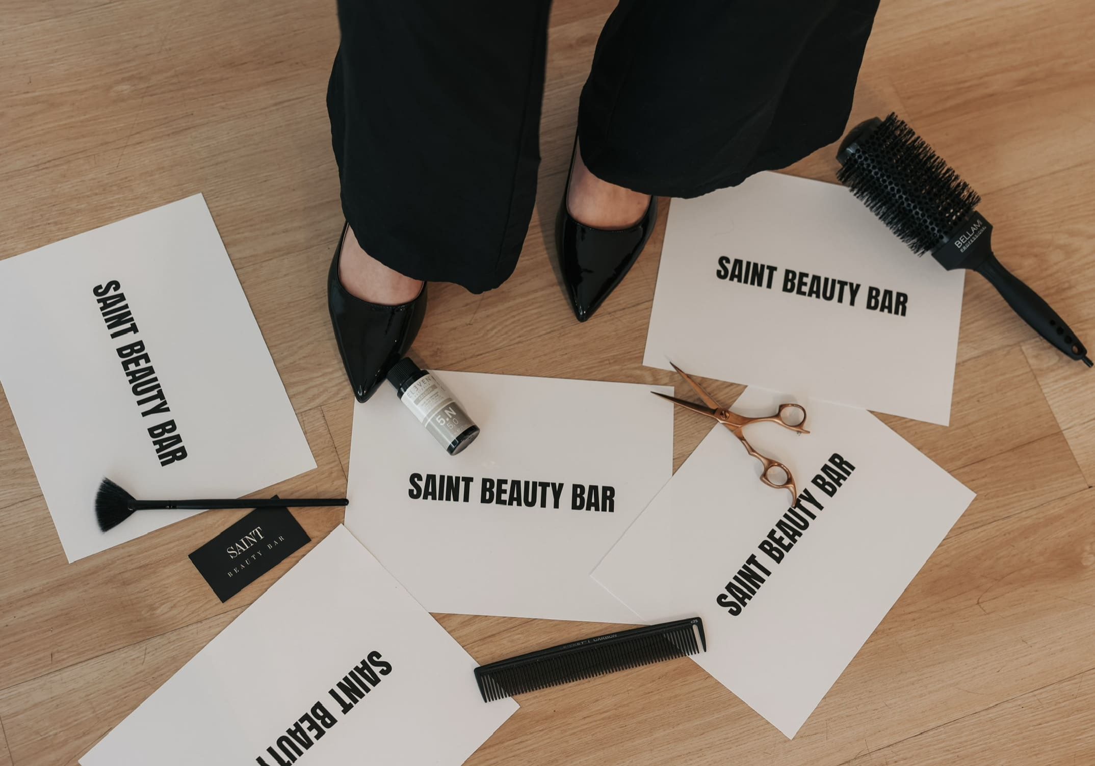 Saint Beauty Bar Scattered hair styling tools on floor over printed Saint Beauty Bar images
